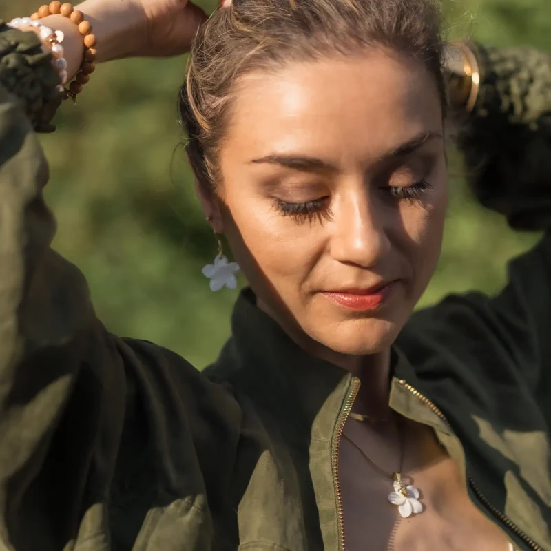 Boucle d'oreille - Fleur de Nacre Femme portant une boucle d'oreille nacre en forme de fleur, un pendentif en nacre et ses bracelets assortis. Des bijoux faits main par DENADDA.