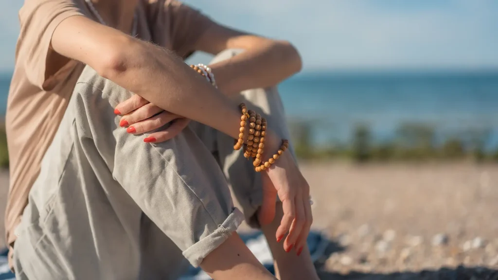Elma contemple l'océan avec ses bracelets de perles de palo santo. Un bijou DENADDA.